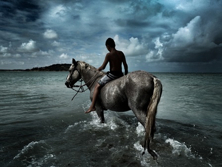 Garoto montado em um cavalo contemplando o mar. Ao fundo vê-se nuvens de tempestade.